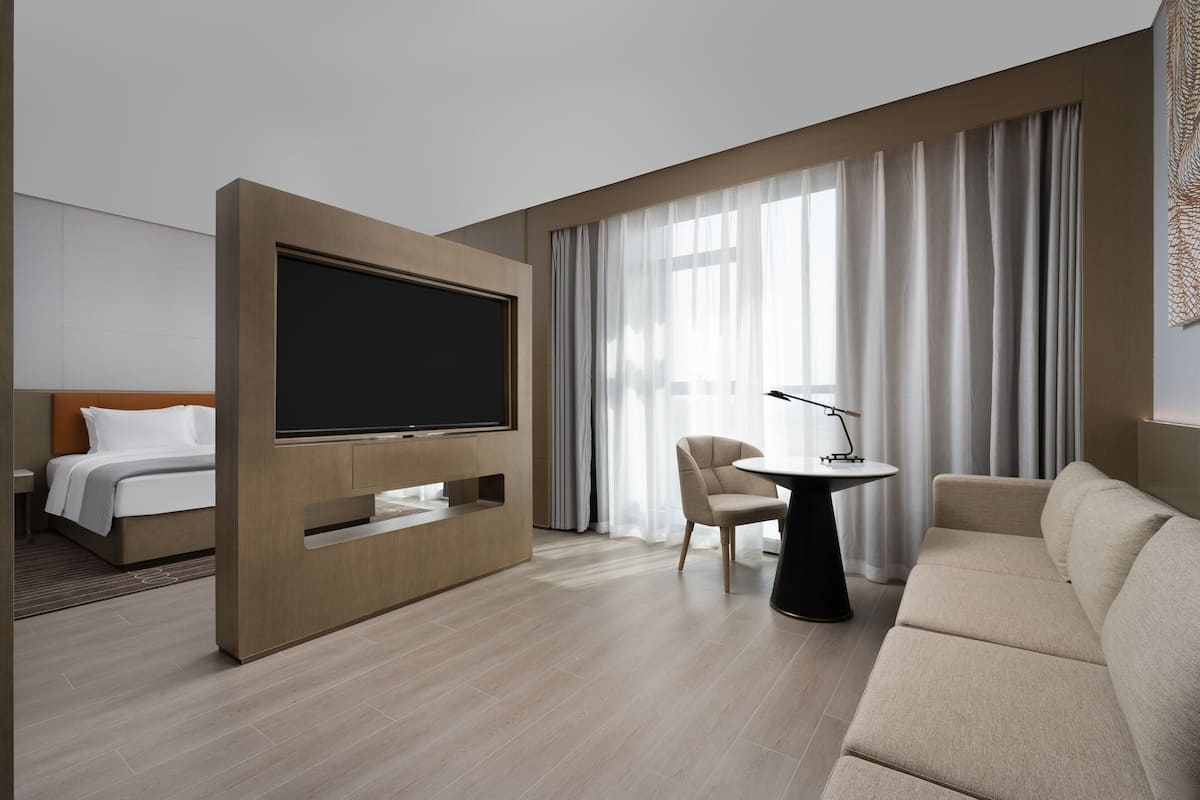 Una habitación de hotel moderna con cama, televisión, sofá, sillón y una mesita.