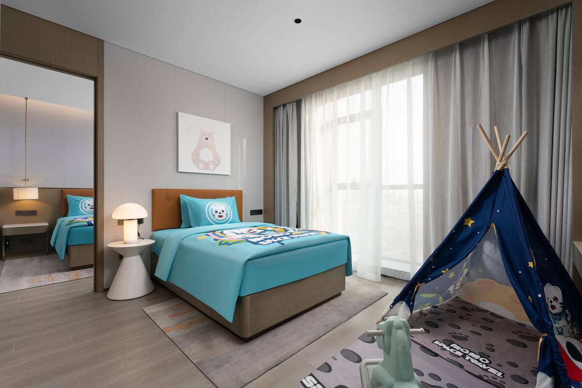 Una habitación de hotel moderna con cama, mesita de noche, lámpara y una estructura azul parecida a una tienda de campaña.