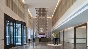 Eine großzügige Lobby mit einer zentralen Rezeption, großen Glastüren und einer modernen Chandelier.