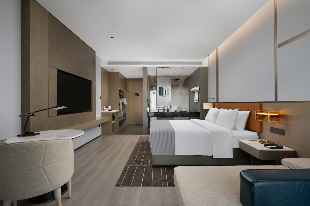 Una habitación de hotel moderna con una cama grande, mesitas de noche, un escritorio, una silla y un televisor.