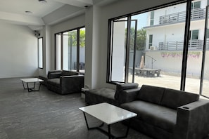 Un interior moderno con ventanas amplias, un sofá, una mesa de centro y un balcón con mobiliario exterior.