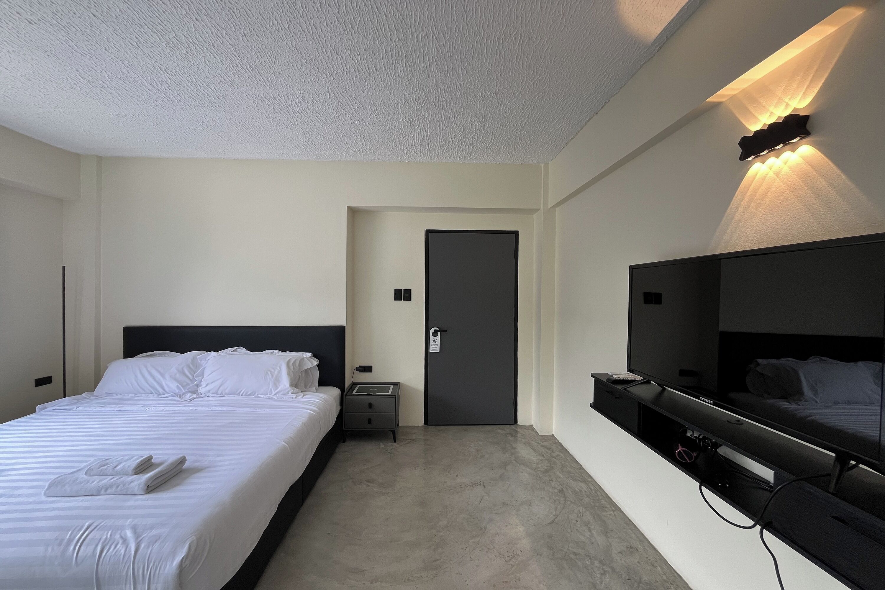 A hotel room with a bed, bedside table, nightstand, and a built-in TV.