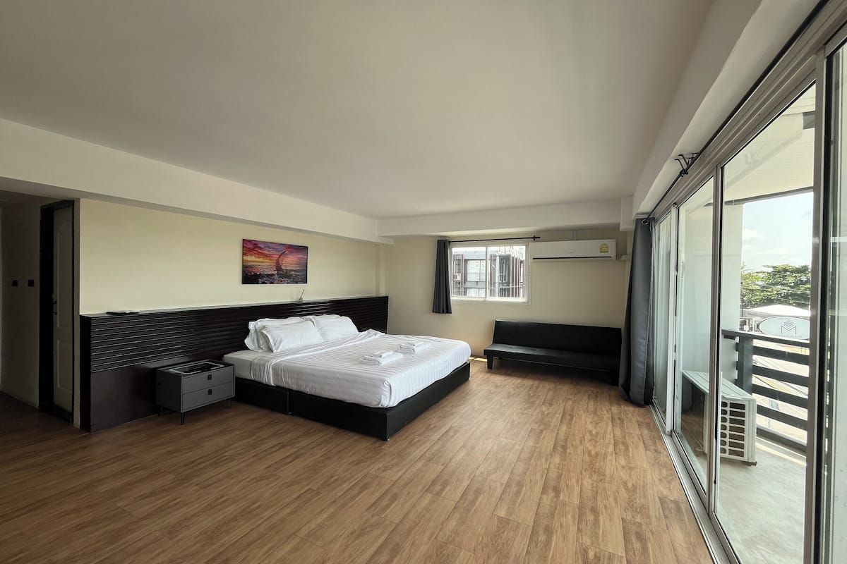 Una habitación de hotel moderna con una cama grande, un banco, un cuadro, un ventanal y un balcón.