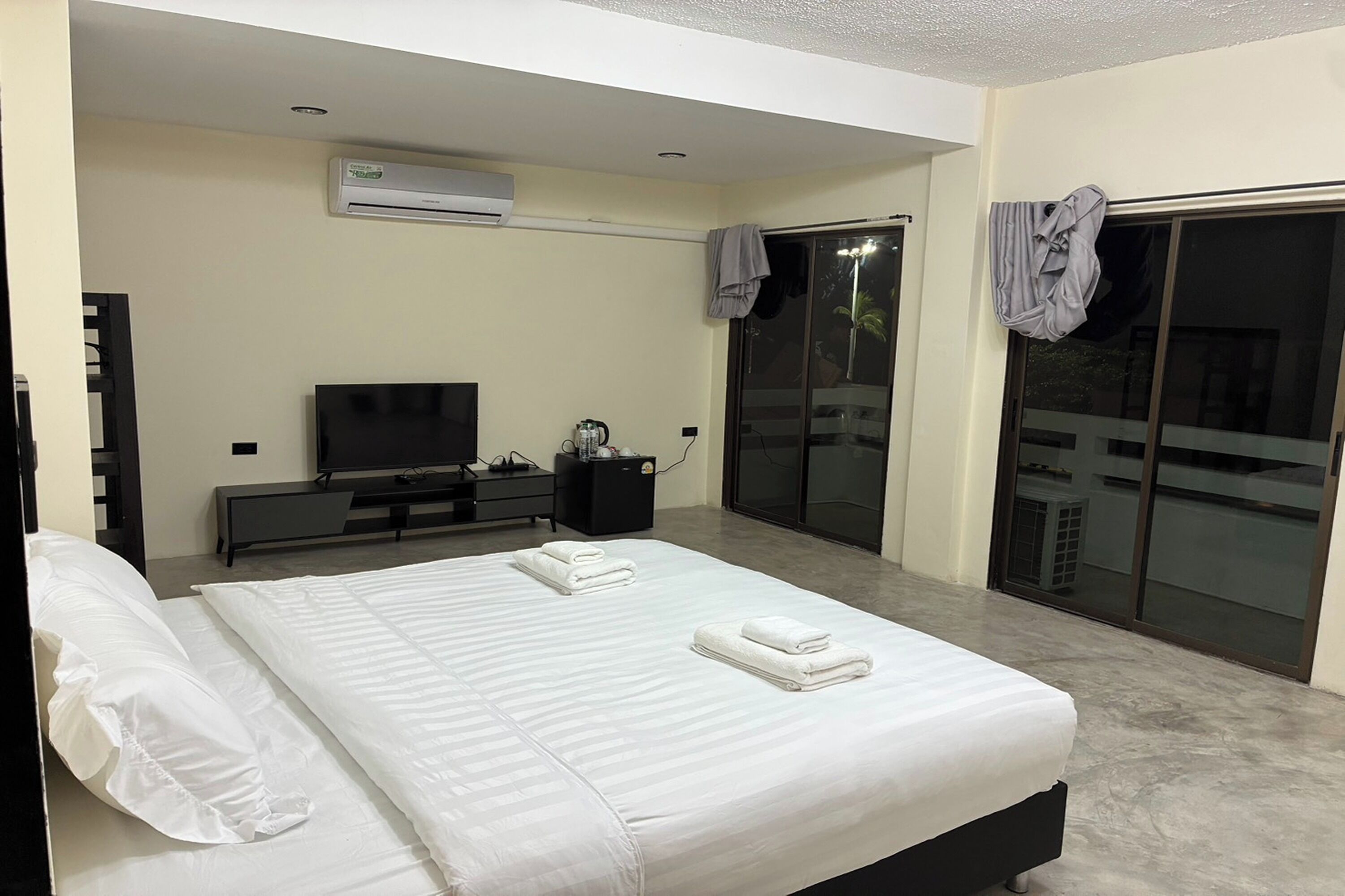 A modern hotel room with a bed, a flat-screen TV, a coffee maker, and a sliding glass door to the outside.