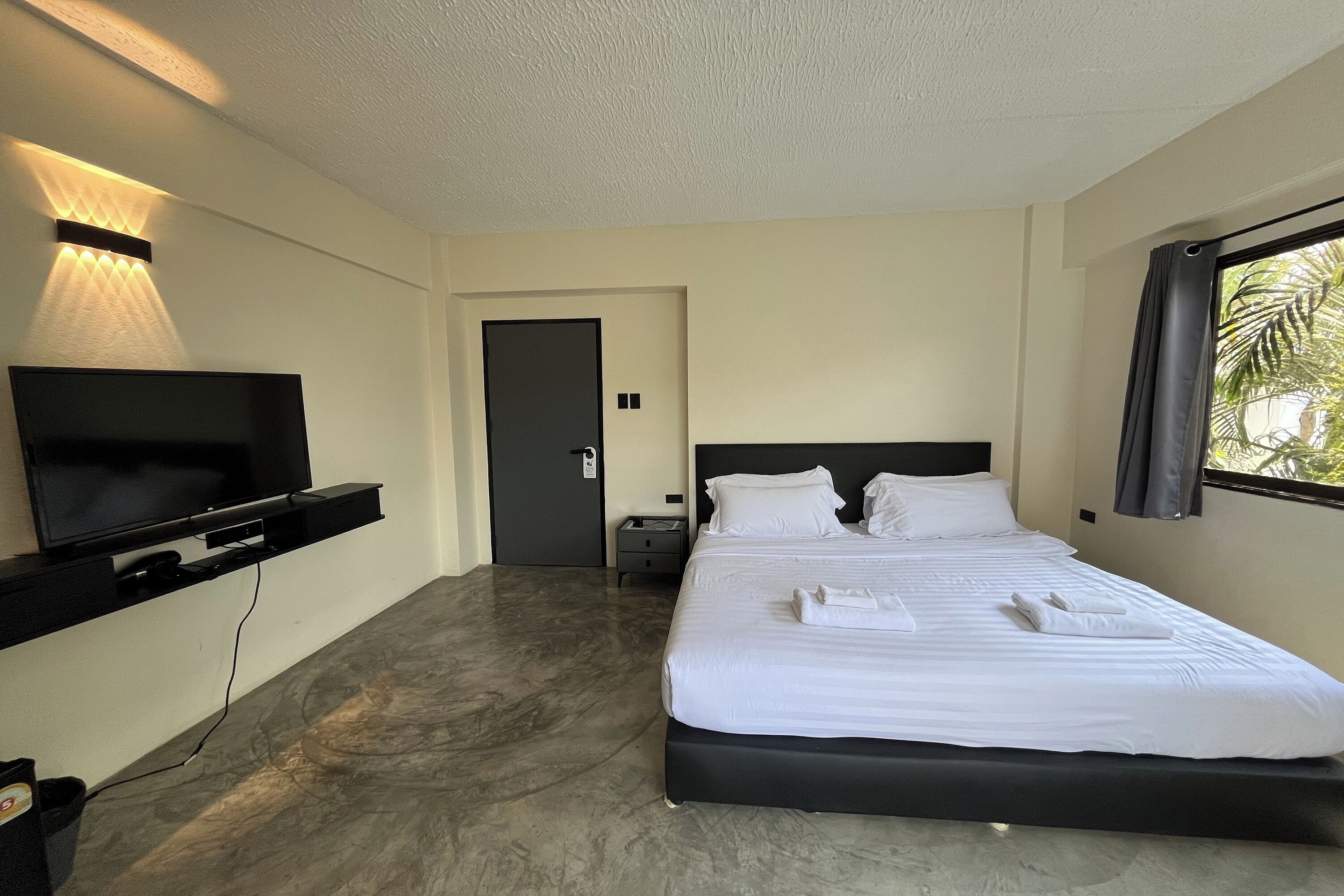 A hotel room with a bed, a TV, a flat-screen TV mounted on the wall, a door, and a window with curtains.