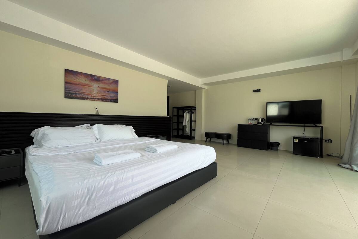 Una habitación de hotel moderna con una cama grande, un televisor de pantalla plana, un escritorio y un cuadro en la pared.