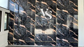 Un mur orné d’un motif de marbre noir et doré, sur lequel on peut voir un panneau avec les lettres « VS » et les mots « Beach Front » écrits.