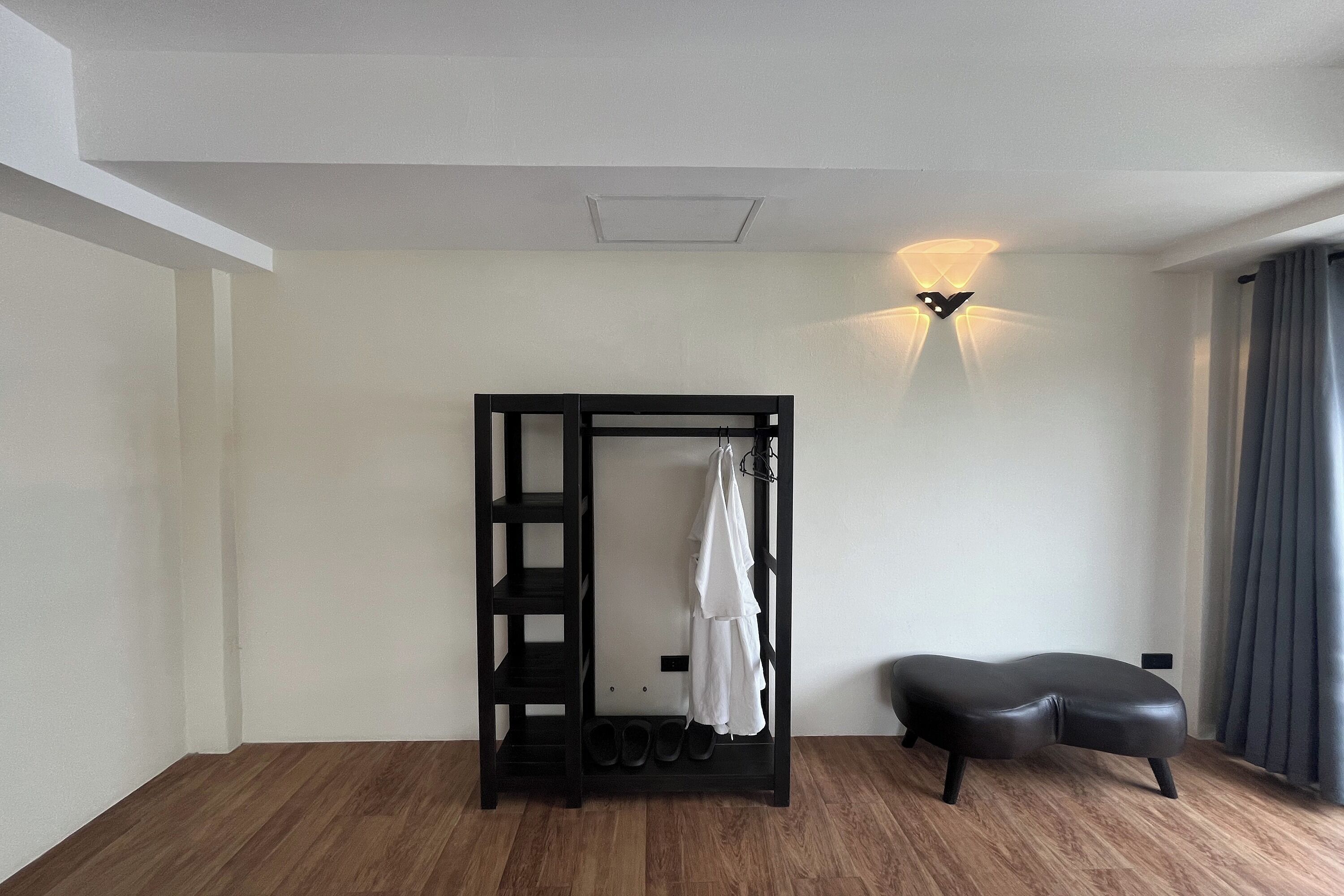 A room with a black bench, a wall-mounted shoe rack, and a wall light fixture.
