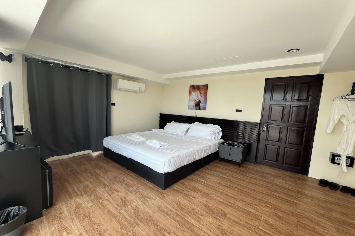 Una habitación de hotel con cama, escritorio, televisor, perchero y puerta.