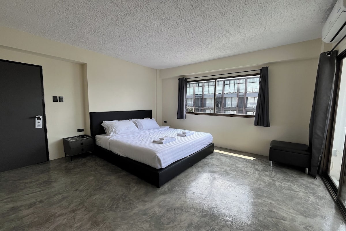 Una habitación de hotel con cama, mesita de noche, ventana con cortinas y puerta.