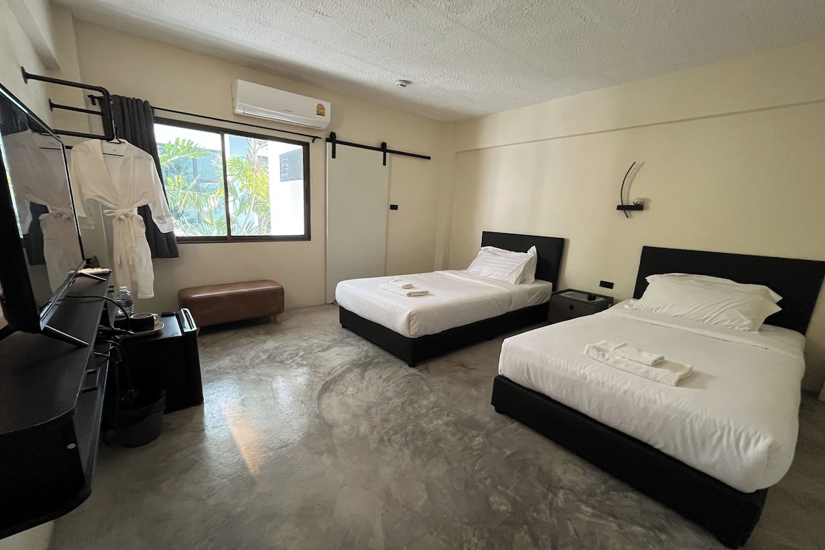 Habitación de hotel con dos camas, un escritorio, una silla, un banco y una ventana con vistas.