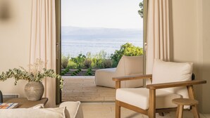Quarto com vista para o mar, uma cadeira de madeira, uma mesa com um vaso e um candeeiro suspenso.