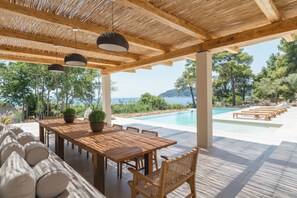 An outdoor patio with a wooden table and chairs, a pool, and a view of the sea. - Villa Delta Skiathos (Skiathos)