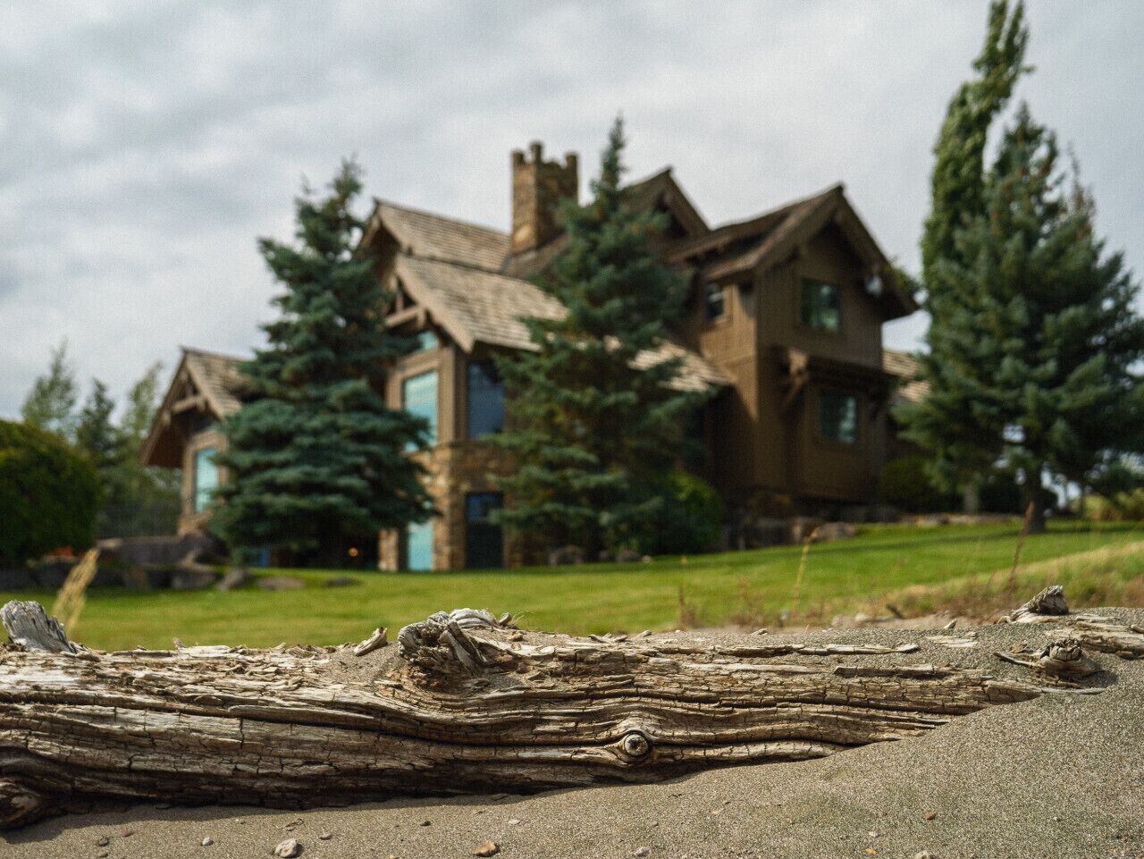 Une maison de campagne au style rustique, dotée d’une cheminée imposante, entourée d’arbres et d’une pelouse verdoyante.