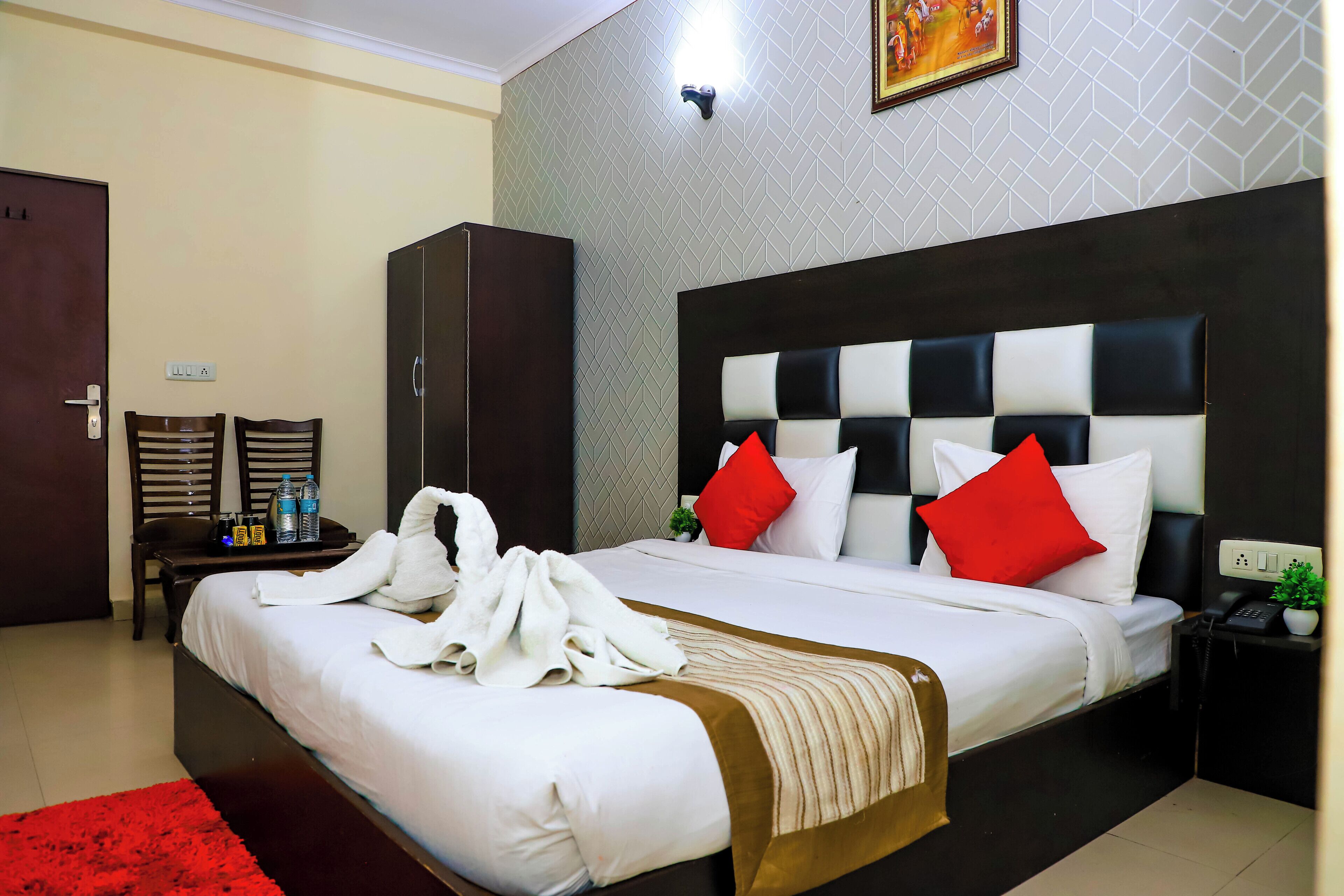 A hotel room with a large bed, a wardrobe, a nightstand with a phone, and a red rug.