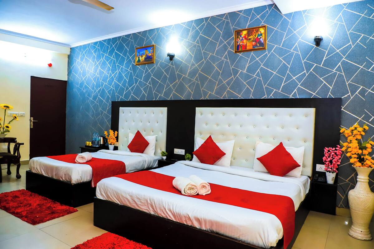 Quarto de hotel com duas camas, roupa de cama vermelha e branca, um tapete vermelho e uma parede com padrão geométrico.