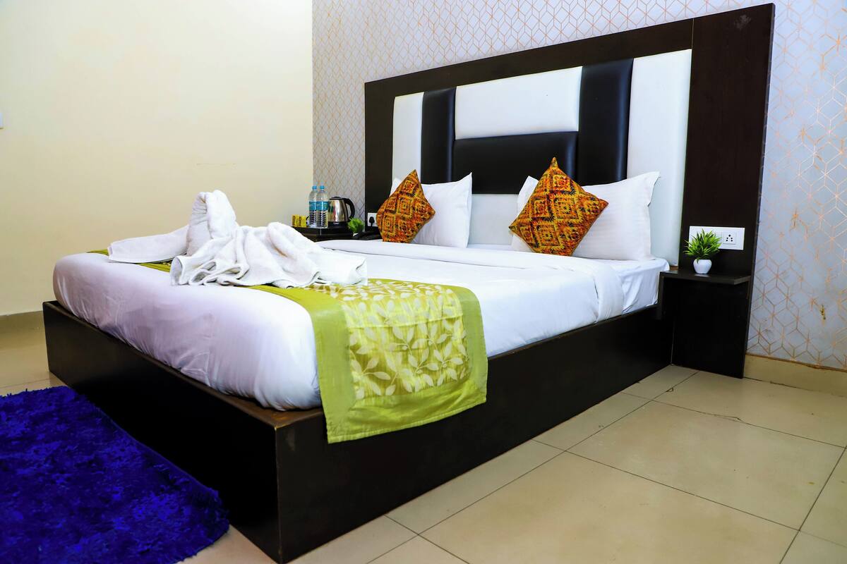 Uma cama bem arrumada com colcha floral verde, almofadas brancas e um tapete azul.