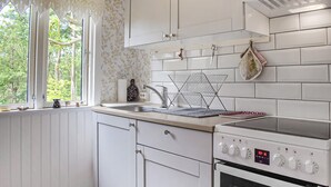 A kitchen with white cabinets, a stainless steel sink, a stove, and a window with a view of trees. - 1 bedroom cozy home in Blentarp (Blentarp)