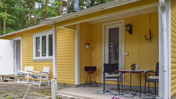 A yellow house with a porch, two white chairs, a table, and a black chair. - 1 bedroom cozy home in Blentarp (Blentarp)