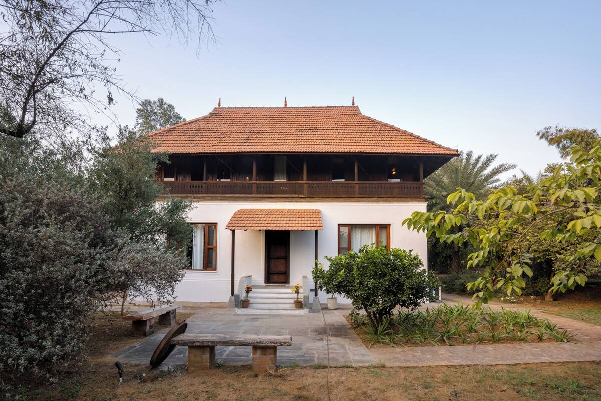 A two-story house with a tiled roof, a front porch, and a garden with a bench and potted plants.