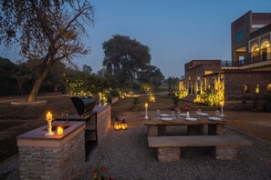 An outdoor dining area with a brick table and benches, surrounded by a garden with trees and plants. - Sadhrana Bagh (Gurugram)