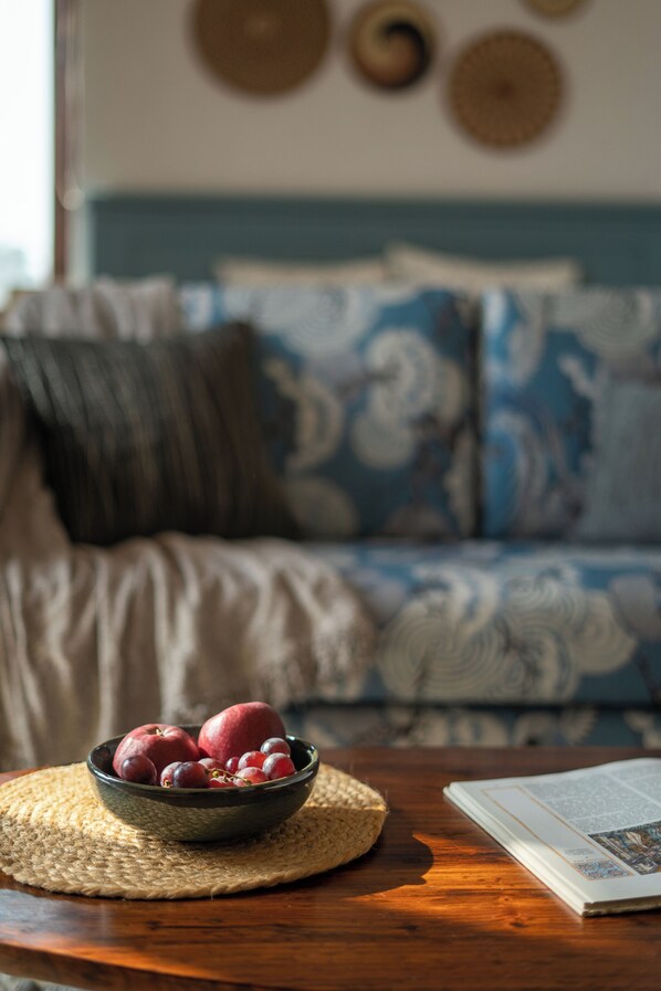 A bowl of fruit on a woven placemat on a wooden table, with a book beside it. - Sadhrana Bagh (Gurugram)