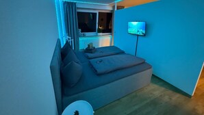 A modern bedroom with a bed, a TV, and LED strip lighting.