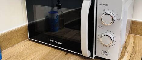 Un horno microondas con pantalla digital, un botón de encendido y una perilla para programar el tiempo.