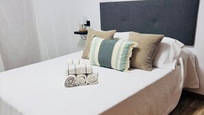 Ein ordentlich bezogenes Bett mit weißer Daunendecke, mehreren Kissen in verschiedenen Farben und Texturen sowie aufgerollten Handtüchern.