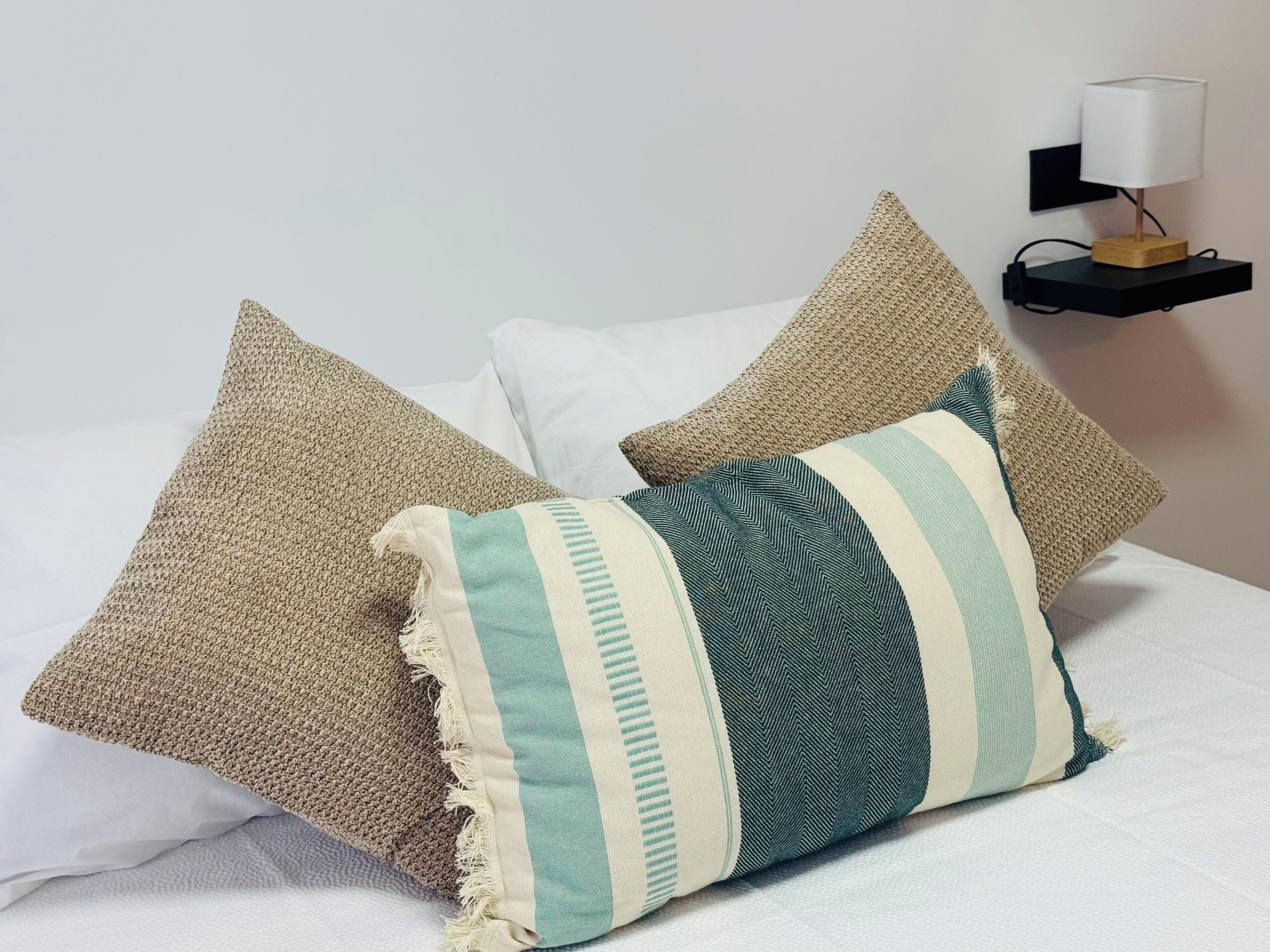 A bed with three pillows and a bedside table with a lamp.