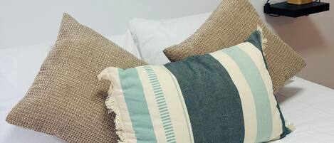 A bed with three pillows and a bedside table with a lamp.