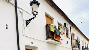 Ein weißes Gebäude mit einer Holztür, einem Balkon mit bunten Flaggen und einer Straßenlaterne.