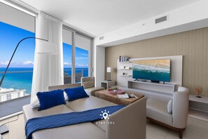 A modern hotel room with a large balcony, a sofa, a TV, and a wooden coffee table. - Stunning 1BR Apt With Ocean View Balcony (Hollywood)
