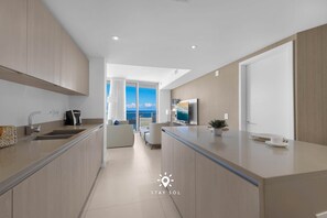 A modern kitchen with a central island, a dining area with a view, and a living space with a sofa and a TV. - Stunning 1BR Apt With Ocean View Balcony (Hollywood)