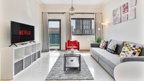 Een moderne woonkamer met een flatscreen televisie, een grijze bank, een rode fauteuil en een salontafel.