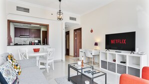 Een moderne woonkamer met een flatscreen televisie, een salontafel, een bank en een eethoek, met een keuken op de achtergrond.