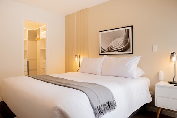 Una cama bien hecha con un plaid gris, una obra de arte abstracta enmarcada en la pared y una lámpara de noche.