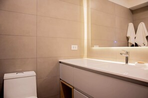 Un baño moderno con un lavamanos blanco, un espejo y dos toallas colgadas en la pared.