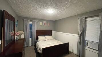 A bedroom with a bed, a dresser, a mirror, a window with curtains, and a ceiling light.