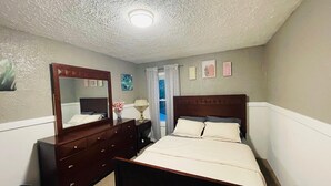 Une chambre à coucher avec un lit en bois, une commode, un miroir, une table de chevet et un luminaire au plafond.