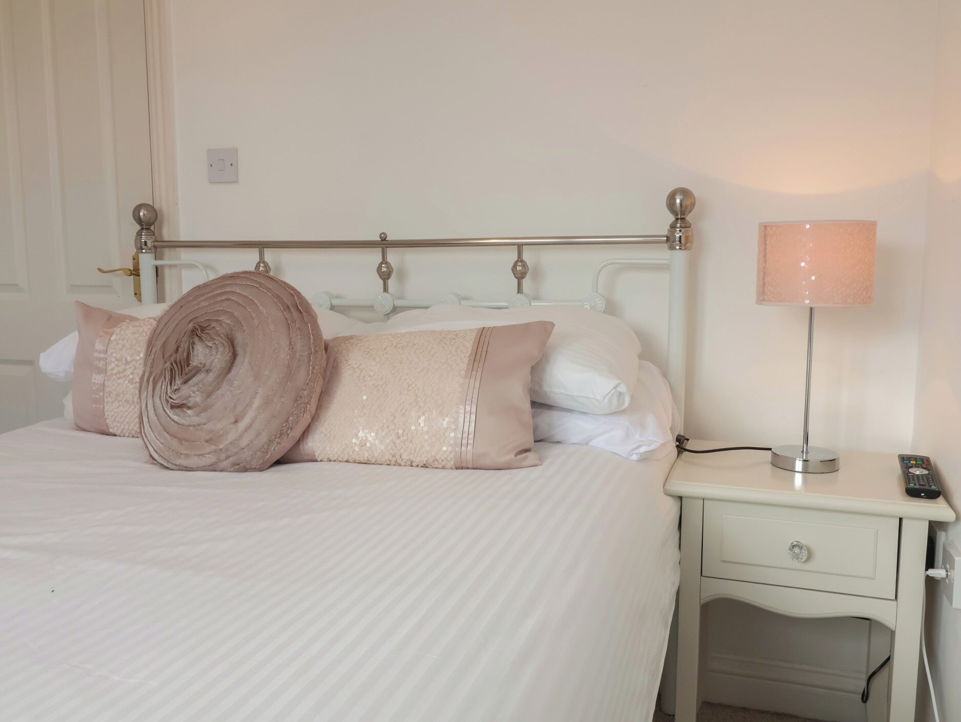 A neatly made bed with a rolled towel, a bedside lamp, and a nightstand with a remote control.
