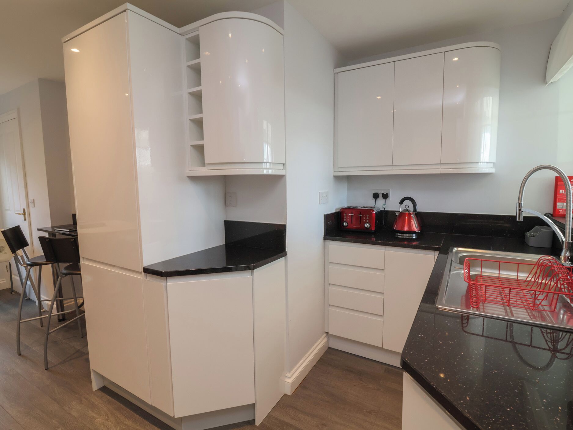 A modern kitchen with white cabinetry, a black countertop, and a red kettle.