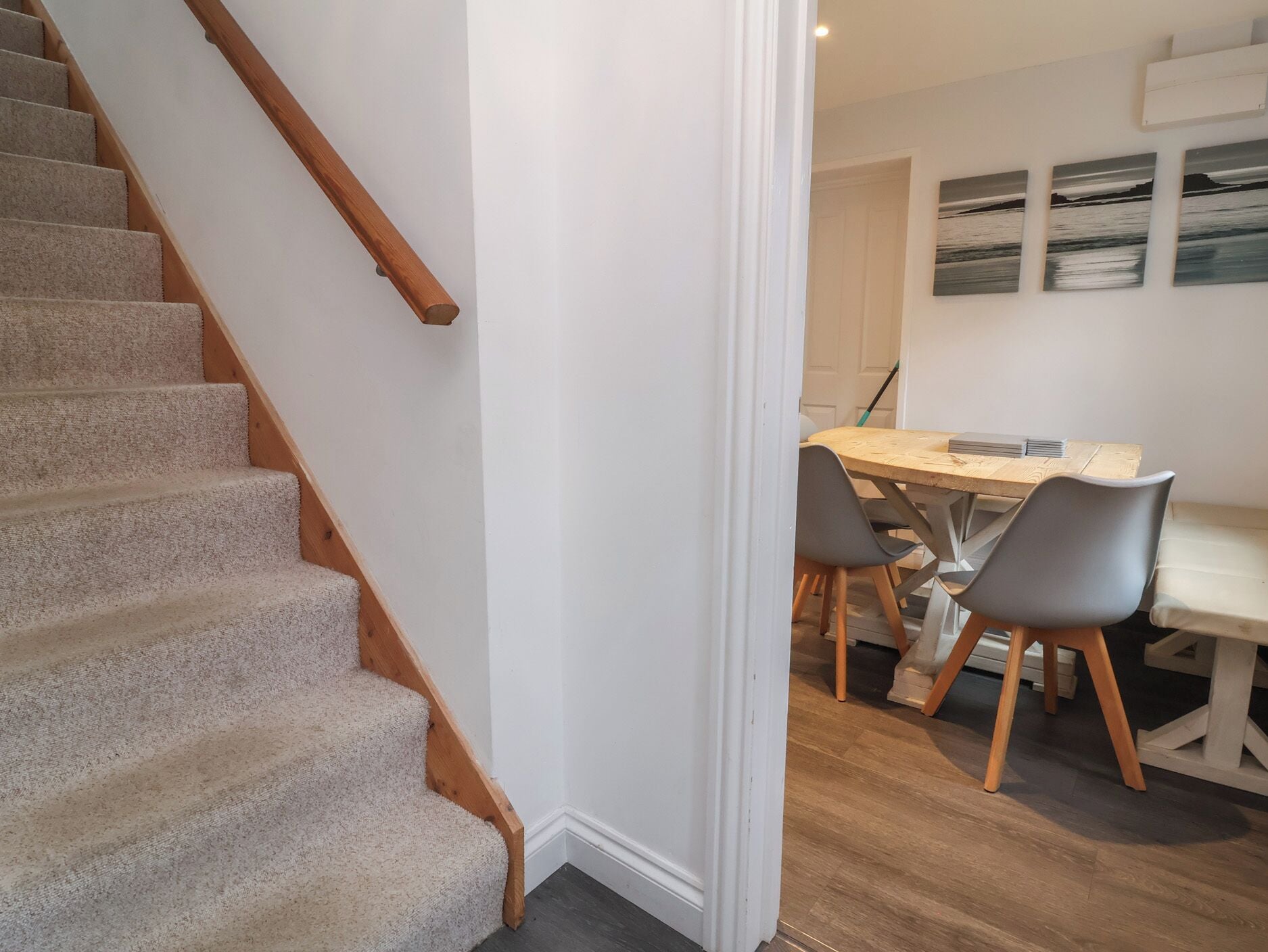 A staircase with carpeted steps and wooden handrails leading to a dining area with a wooden table and two chairs.
