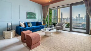 A modern living room with a blue sofa, a round coffee table, and a view of a city skyline through large windows. - Downtown Views (Dubai)
