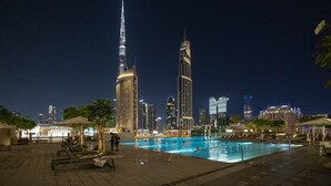 A nighttime view of a pool area with a city skyline in the background, including a prominent skyscraper. - Downtown Views (Dubai)