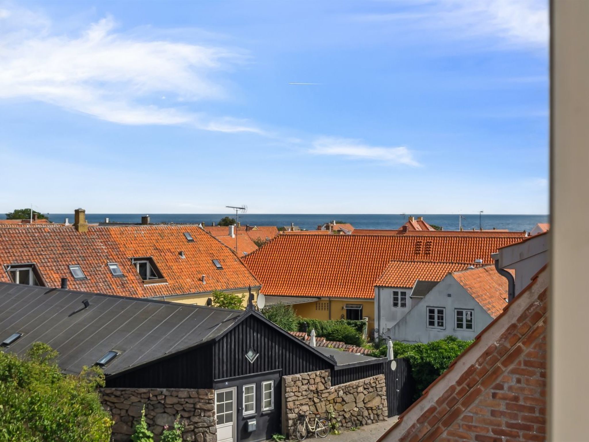 A coastal town with terracotta-roofed buildings, a stone wall, and a view of the sea.