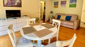 A dining area with a round table and chairs, a sofa, a TV, and artwork on the walls. - Studio apartment with garden in San Siro (Milano)