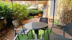 An outdoor patio with a round table and four chairs, surrounded by greenery and a building in the background. - Studio apartment with garden in San Siro (Milano)