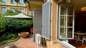 A patio with a potted plant, a large umbrella, and a window with shutters. - Studio apartment with garden in San Siro (Milano)