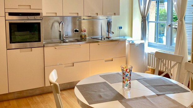 A modern kitchen with stainless steel appliances, a round dining table with placemats, and a window with curtains. - Studio apartment with garden in San Siro (Milano)